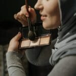 Kobieta w hidżabie nakłada pędzlem makijaż dzienny w domu