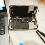 Rozkręcony iPhone obok narzędzi i laptopa podczas samodzielnej naprawy