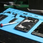 Rozłożony smartfon z częściami i narzędziami na niebieskiej macie serwisowej