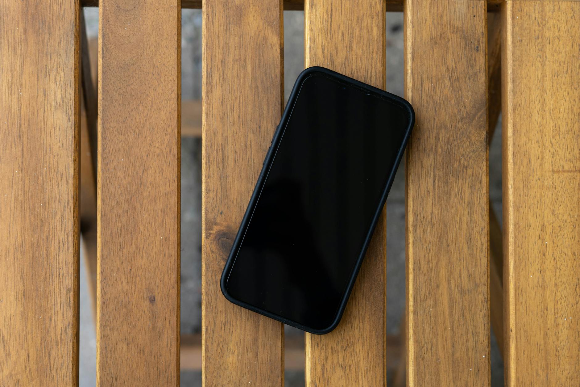 Smartfon z wygaszonym ekranem leży na drewnianym stole