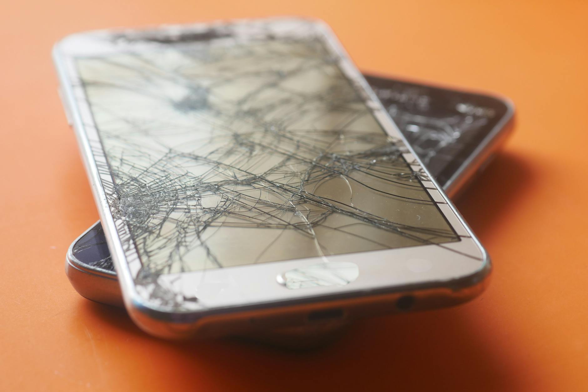Dwa uszkodzone smartfony z pękniętymi ekranami na pomarańczowym tle