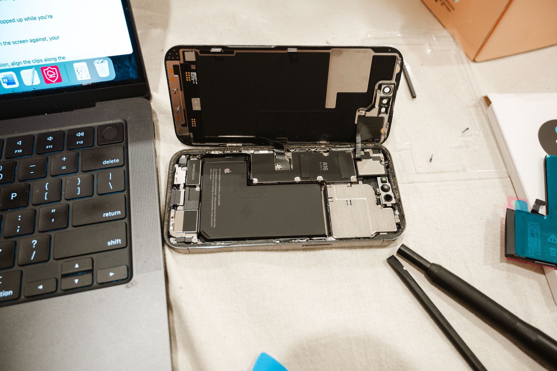 Otwarty iPhone obok narzędzi serwisowych i laptopa podczas wymiany baterii