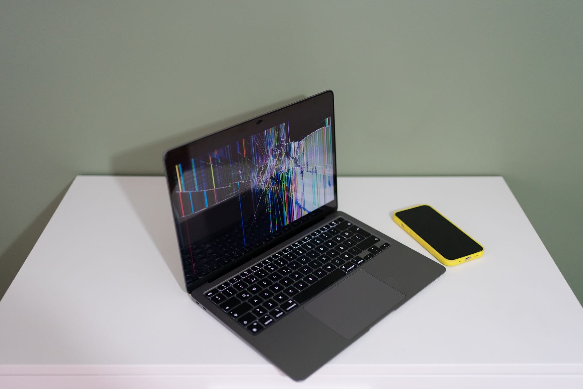 Uszkodzony ekran laptopa z kolorowymi liniami obok żółtego smartfona