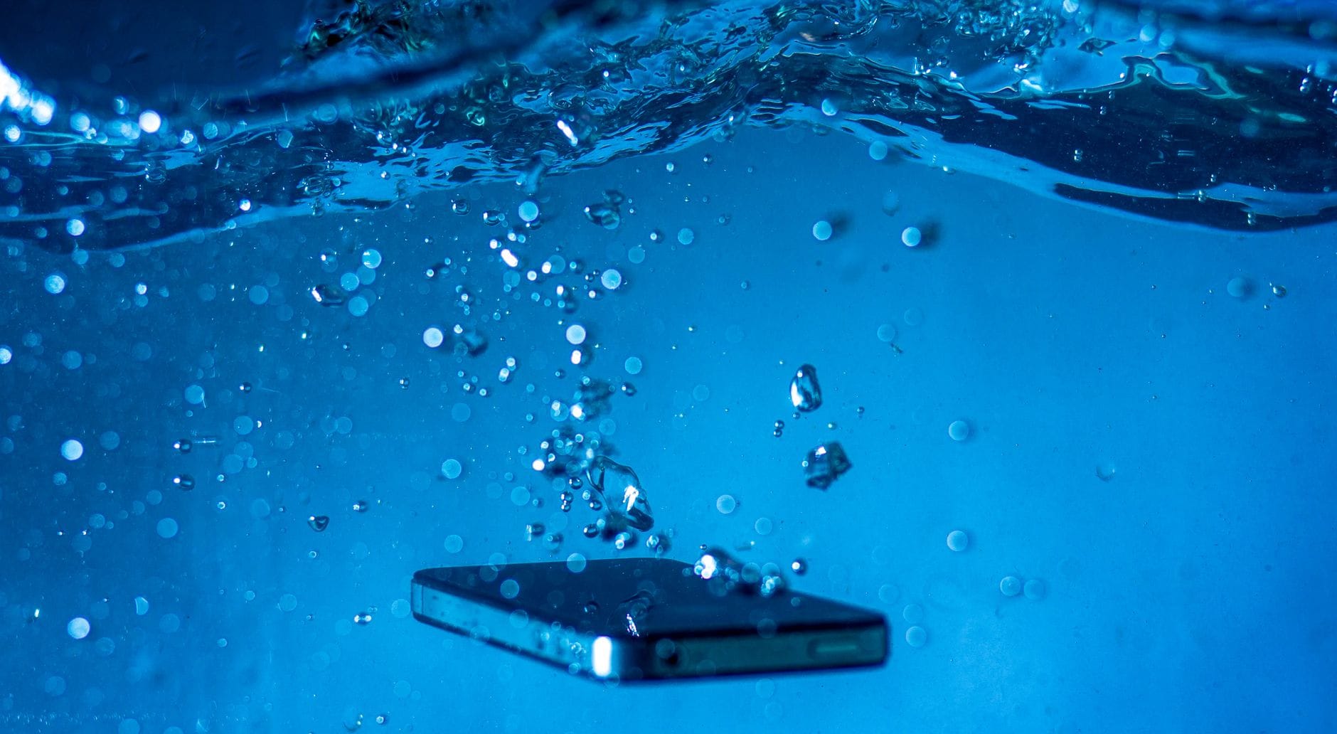 Co naprawdę dzieje się z elektroniką telefonu po zalaniu wodą lub napojem Smartfon zanurzony w wodzie z unoszącymi się bąbelkami